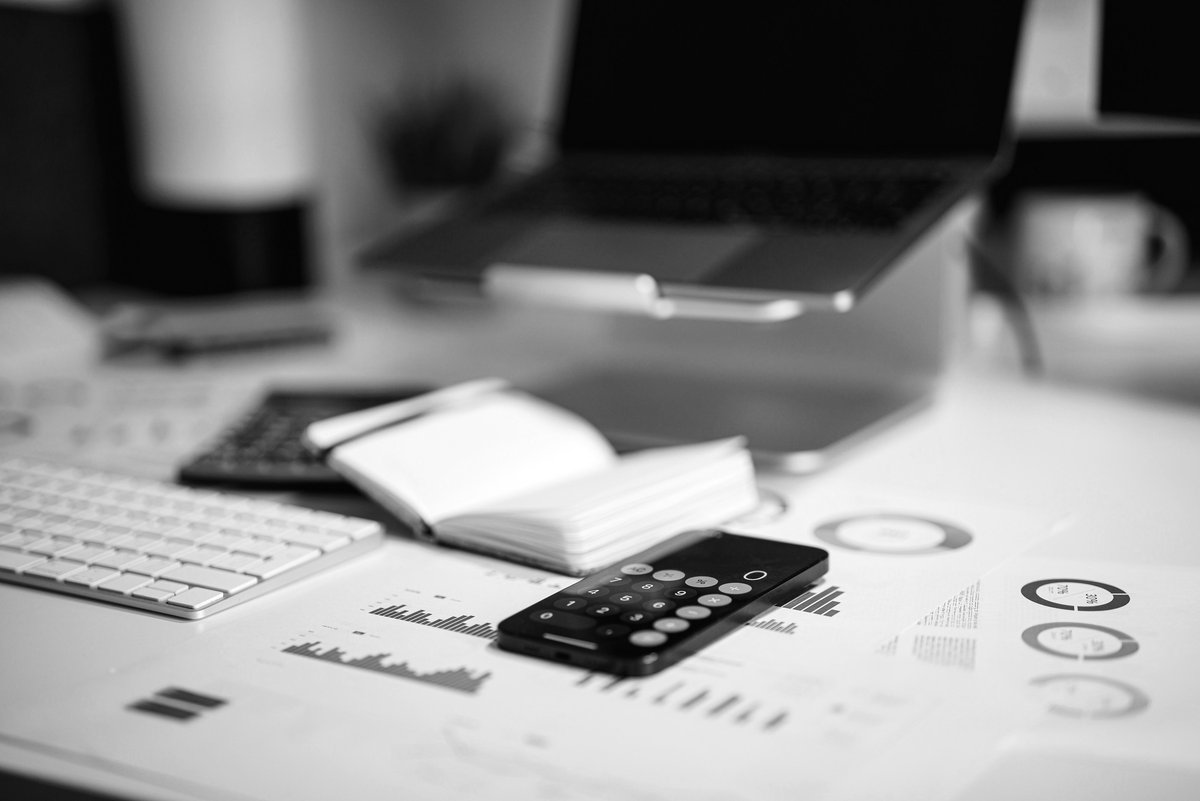 Calculator app on a phone resting on a desk with financial charts