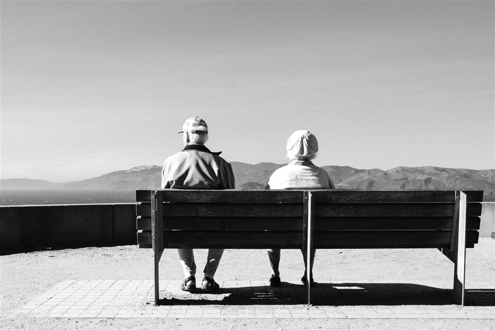 An older couple on a bench overlooking a wide coastal view