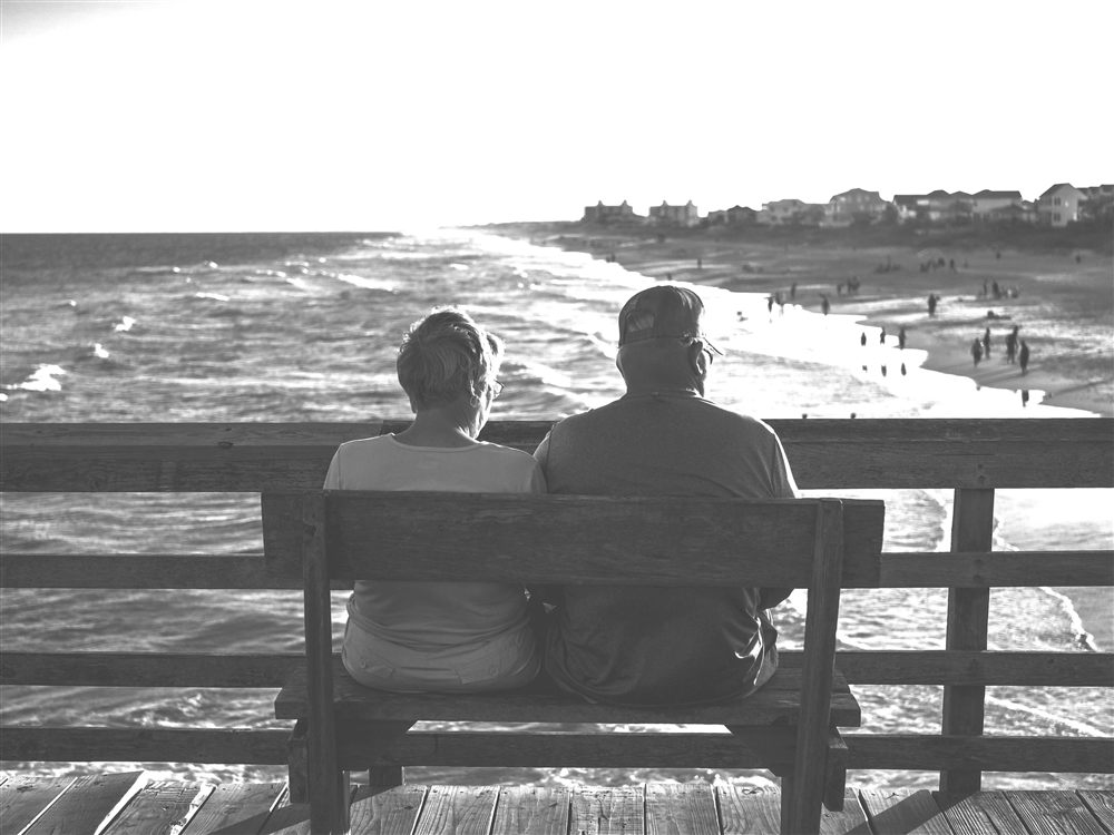A retired couple sitting close together on a bench by the sea