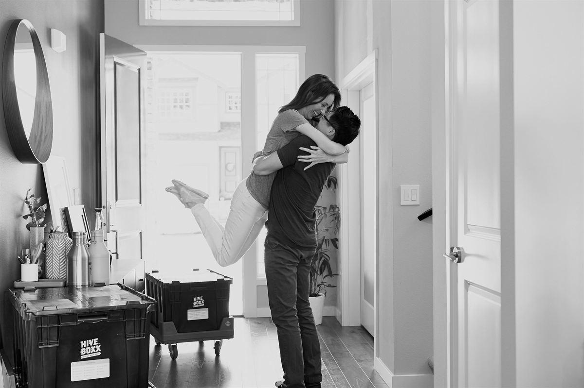 A couple celebrating in the hallway of their new home, surrounded by moving boxes